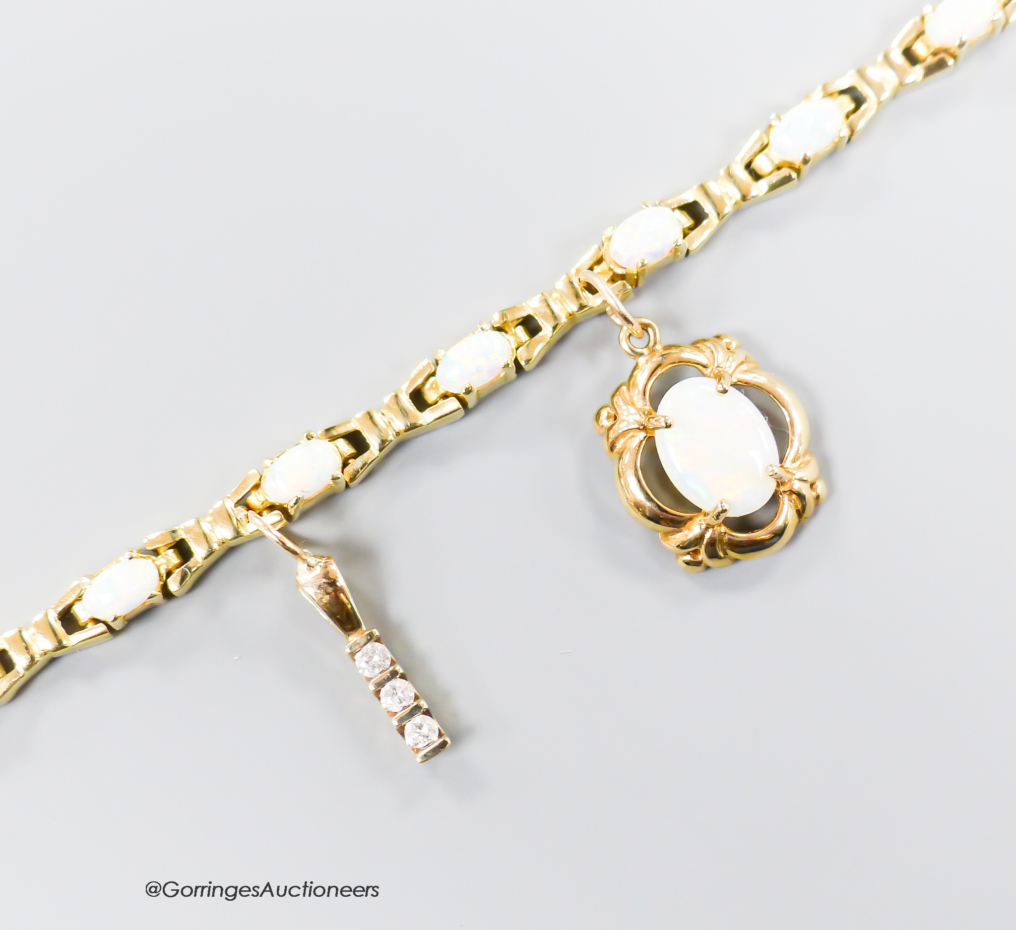 A modern 585 yellow metal and oval white opal set bracelet, hung with two yellow metal charms (white opal and three stone diamond), bracelet overall 18.5cm, gross 11.2 grams.